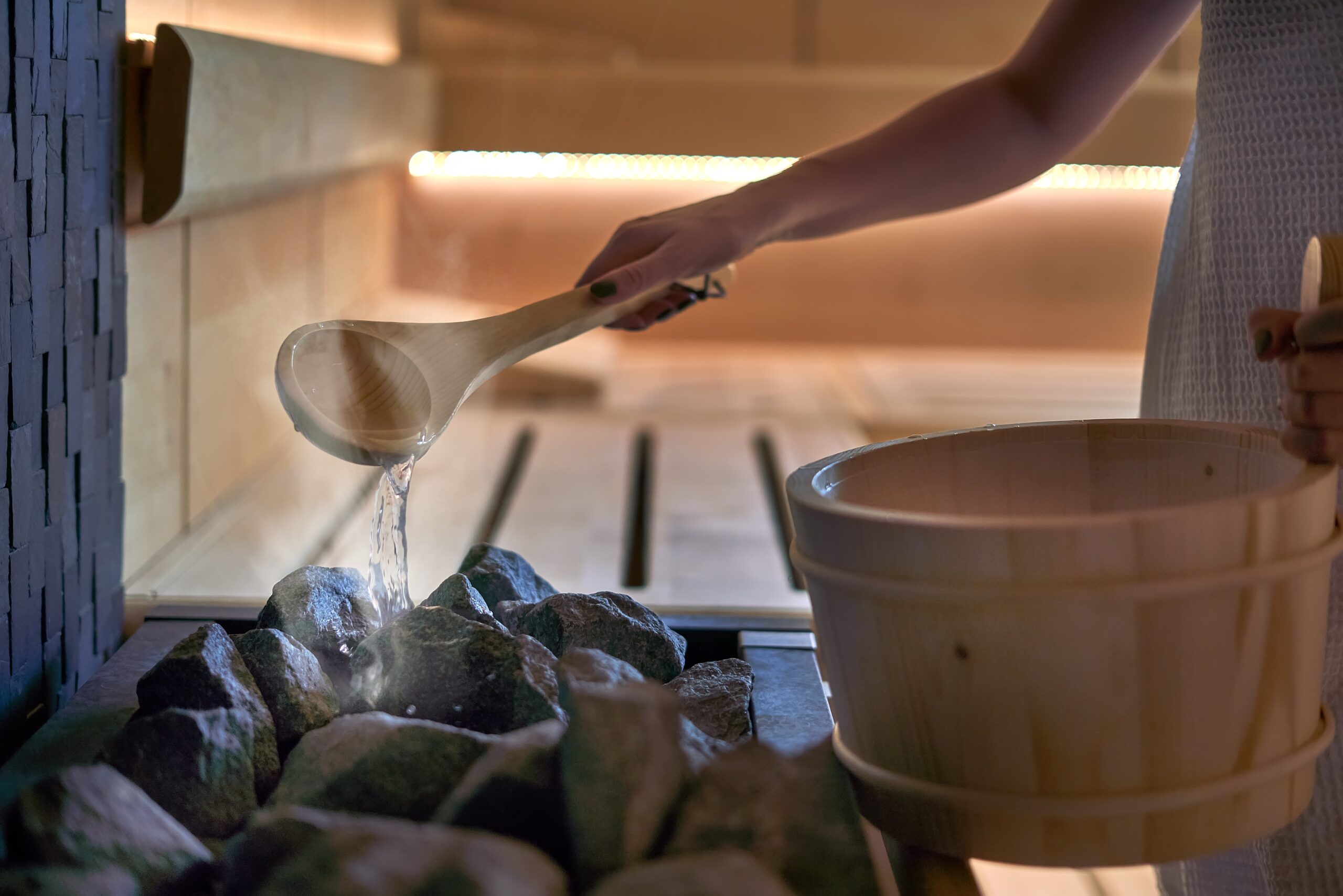 Woman in sauna pouring water to hot stones to produce steam